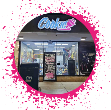 Storefront at night that has a lit up sign that says 'Cookie' with an electrical plug in graffiti typograghy with a sing that says 'Coming Soon'