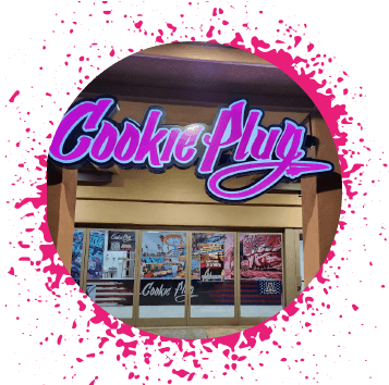 Bright neon pink sign that's lit up that says 'Cookie Plug' on a tan peach building that has large images of cookies and graffiti in the window.