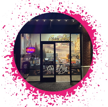 Brick store front with a golden yellow sign that says 'Cookie Plug' with cookie racks in the window and a graffiti boombox.