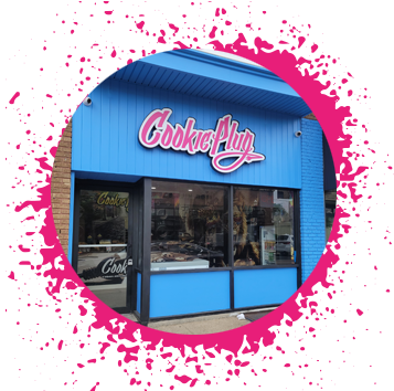 Bright blue storefront with a black, white, and pink graffiti sign that says 'Cookie Plug' that has pictures of cookies on the side of the front counter.
