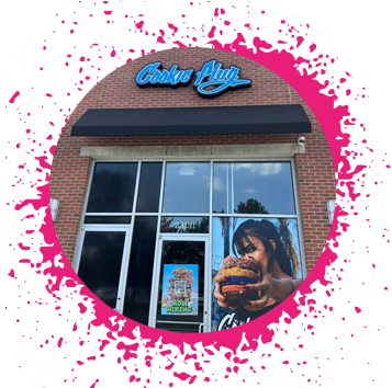 Brick storefront with a blue, white, and black sign that says 'Cookie Plug' that has a large image of a girl who is holding a large stack of cookies in assorted flavors with the logo that says 'Cookie Plug' at the bottom.